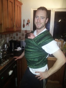 Photo of my husband carrying our daughter in a hybrid stretchy wrap on a December evening