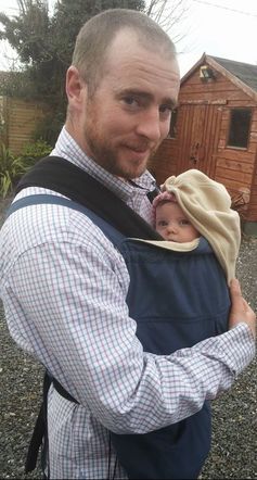 My husband carrying our daughter in a sling covered by a babywearing cover on a spring day