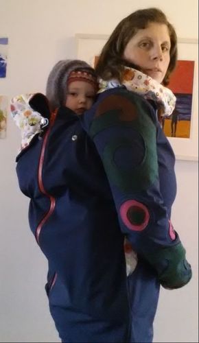 Photo of me wearing my daughter in a sling in a back carry inside a waterproof babywearing jacket.